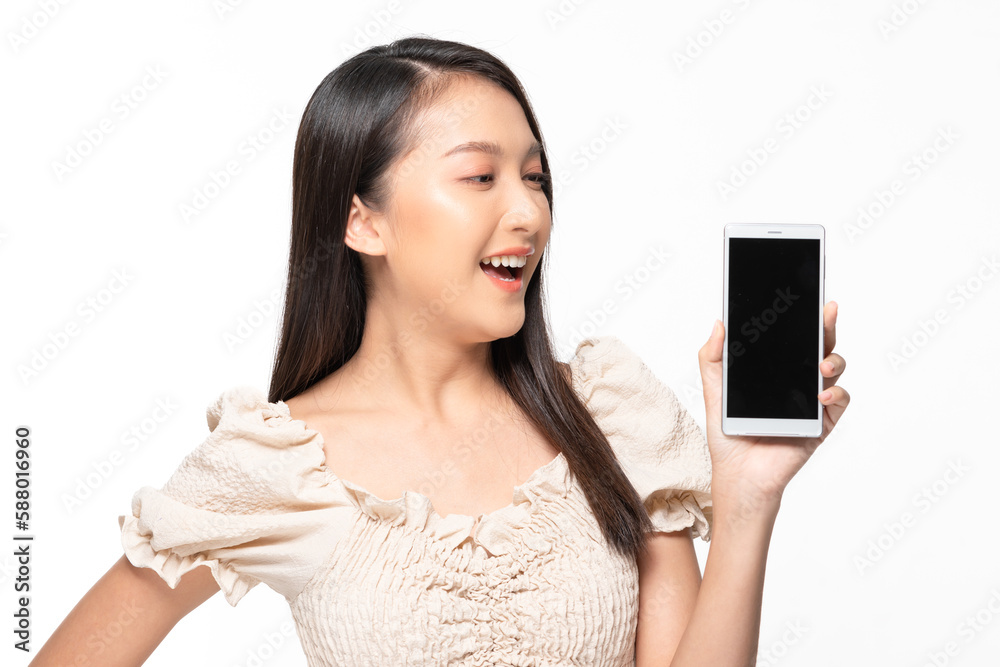 Happy attractive asian young woman smile and showing mobile phone isolated on white background. Cheerful pretty girl wear casual dress raise up smartphone to empty space for mockup to display product Happy attractive asian young woman smile and showing mobile phone isolated on white background. Cheerful pretty girl wear casual dress raise up smartphone to empty space for mockup to display product