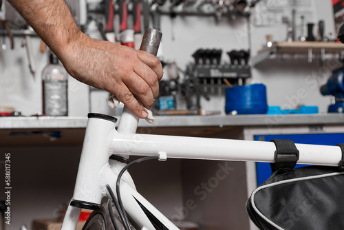 Close up of hand of experienced craftsman, holds pipe from frame of bicycle in repair shop, cleans. Against background of desk with tools in garage, a man's hand holding a part from a bicycle