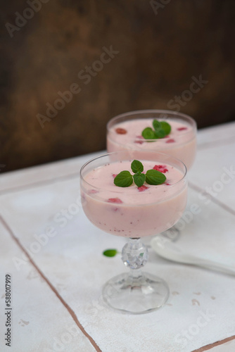 Two glasses with strawberries puding on white table in brown background.