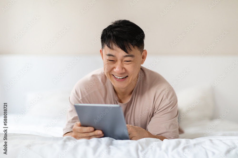 Asian man using nice application on digital tablet, bedroom interior Asian man using nice application on digital tablet, bedroom interior