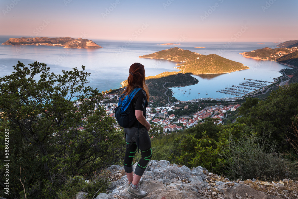 Hiking on Lycian way trail. Young girl with backpack enjoy view of panoramic lansdscape of seaside resort town of Kas. Mediterranean coast. Antalya. Turkey.