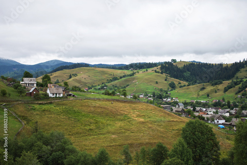 Traditional ukrainian houses in mountain village in summer. Mountain valley in Ukraine. Rural landscape with buildings, green grass, trees on the hill © voloshin311