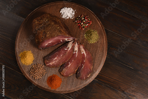 Dried Processed Beef Jerky with spices on wooden board against dark background. Slicing. Top view above, flat lay.