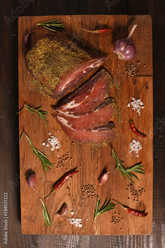 Dried Processed Beef Jerky with spices and vegetables on wooden board. Slicing. Homemade organic. Top above. Vertical.