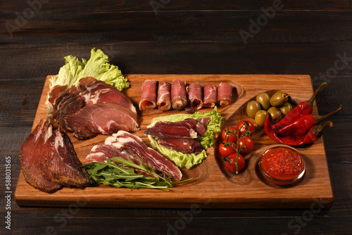 Dried Processed Beef Jerky with spices and vegetables on wooden board against dark background.Slicing. Studio light