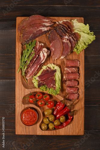 Dried Processed Beef Jerky with spices and vegetables on wooden board against dark background.Slicing.Flat lay. Vertical