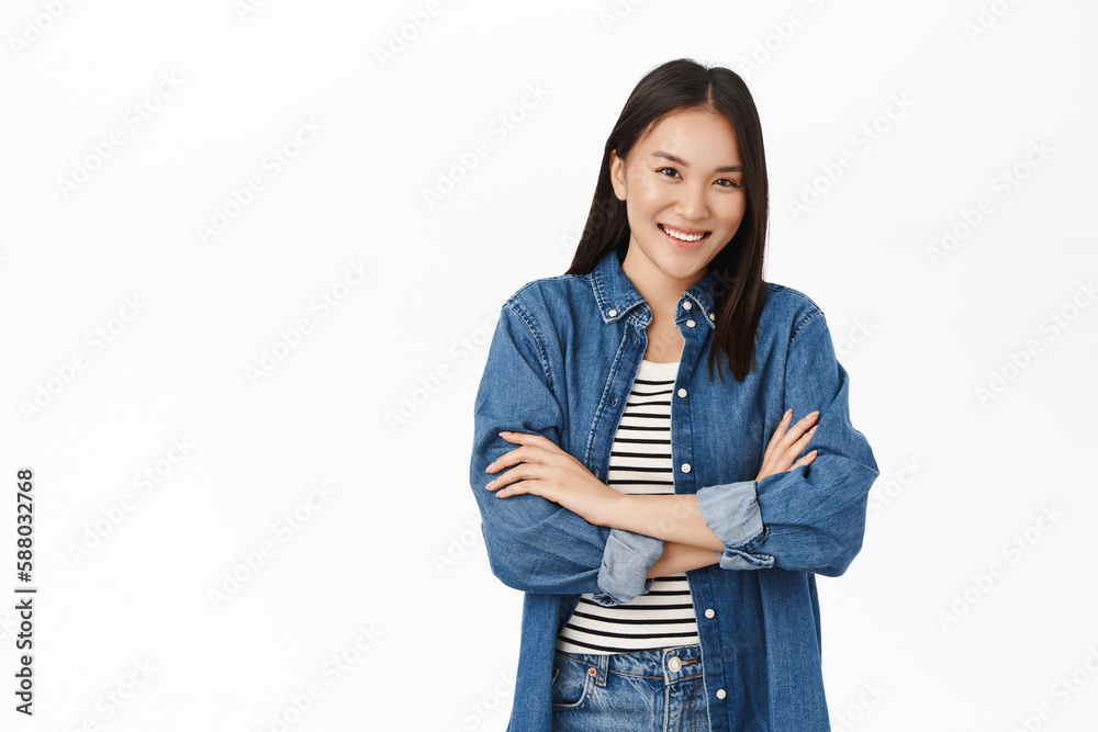 Sassy korean girl, stands in confident pose, smiles and looks self-assured and motivated, white studio background Sassy korean girl, stands in confident pose, smiles and looks self-assured and motivated, white studio background