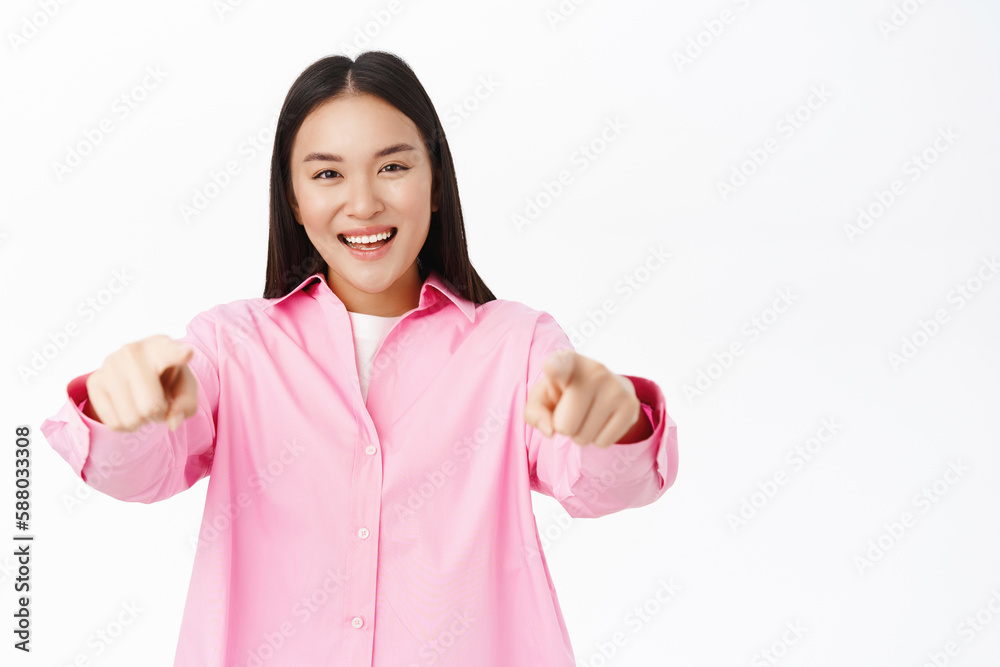 Congrats lucky you. Smiling happy asian girl points at camera, invites people, says her congratulation and praises, stands over white background Congrats lucky you. Smiling happy asian girl points at camera, invites people, says her congratulation and praises, stands over white background