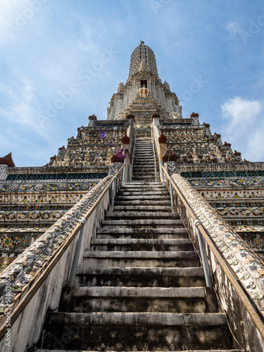 Steep steps leading up the Wat Arun Temple  the Temple of Dawn  in Bangkok  Thailand  with its spire pointing towards a blue sky.