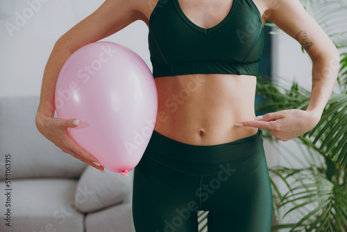Εκτύπωση καμβά Cropped close up young strong sporty athletic fitness trainer instructor woman wear green tracksuit train hold balloon point on belly do exercises at home gym indoor