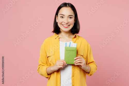 Traveler woman of Asian ethnicity casual clothes hold passport ticket isolated on plain pastel pink background. Tourist travel abroad in free spare time rest getaway. Air flight trip journey concept. #588064344