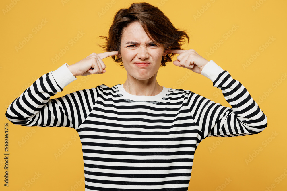 Young mad sad woman wear casual striped black and white shirt cover ears with hands fingers do not want to listen scream isolated on plain yellow color background studio portrait. Lifestyle concept. Young mad sad woman wear casual striped black and white shirt cover ears with hands fingers do not want to listen scream isolated on plain yellow color background studio portrait. Lifestyle concept.