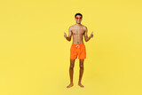 Full body satisfied smiling young sexy man wear orange shorts swimsuit relax near hotel pool showing thumb up like gesture isolated on plain yellow background Summer vacation sea rest sun tan concept