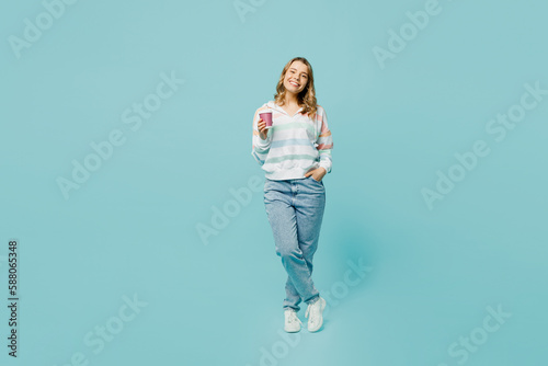 Full body smiling happy young woman wear striped hoody hold takeaway delivery craft paper brown cup coffee to go isolated on plain pastel light blue cyan background studio portrait. Lifestyle concept.