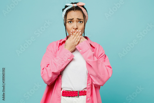 Young shocked scared woman of African American ethnicity wear pink shirt white t-shirt headscarf look camera cover mouth with hands isolated on plain pastel light blue cyan background studio portrait.