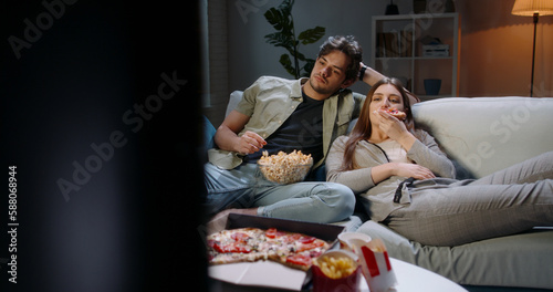 Fotografi Caucasian extremely frustrated couple sitting in front of tv watching shows and eating pizza in absolute boredom