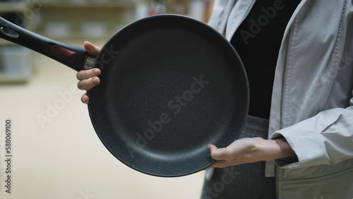 Hands of woman holding a new pan, choosing black teflon frying pan, customer deciding to buy non-stick frying pan for cooking food in her kitchen