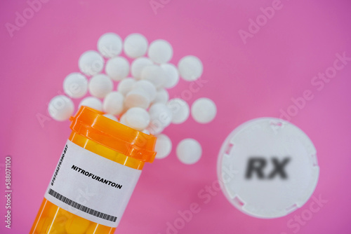 Nitrofurantoin Rx medicine pills in plactic vial with tablets. Pills spilling   from yellow container on pink background. photo
