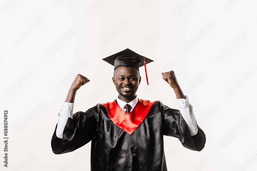 Graduate african man is graduating college and celebrating academic achievement. Happy african student in black graduation gown and cap raises his hands above head on white background. Graduate african man is graduating college and celebrating academic achievement. Happy african student in black graduation gown and cap raises his hands above head on white background.