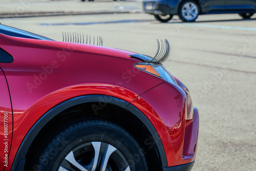 A red car in the mall parking lot has fake eyelashes above the headlights.  Funny accessory for an automobile driven by a woman.  