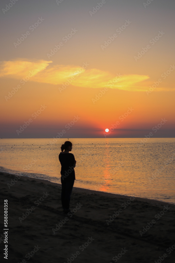 Medium wide shot rear view of woman standing in surf on tropical beach watching sunrise