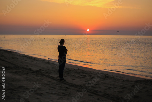 Medium wide shot rear view of woman standing in surf on tropical beach watching sunrise
