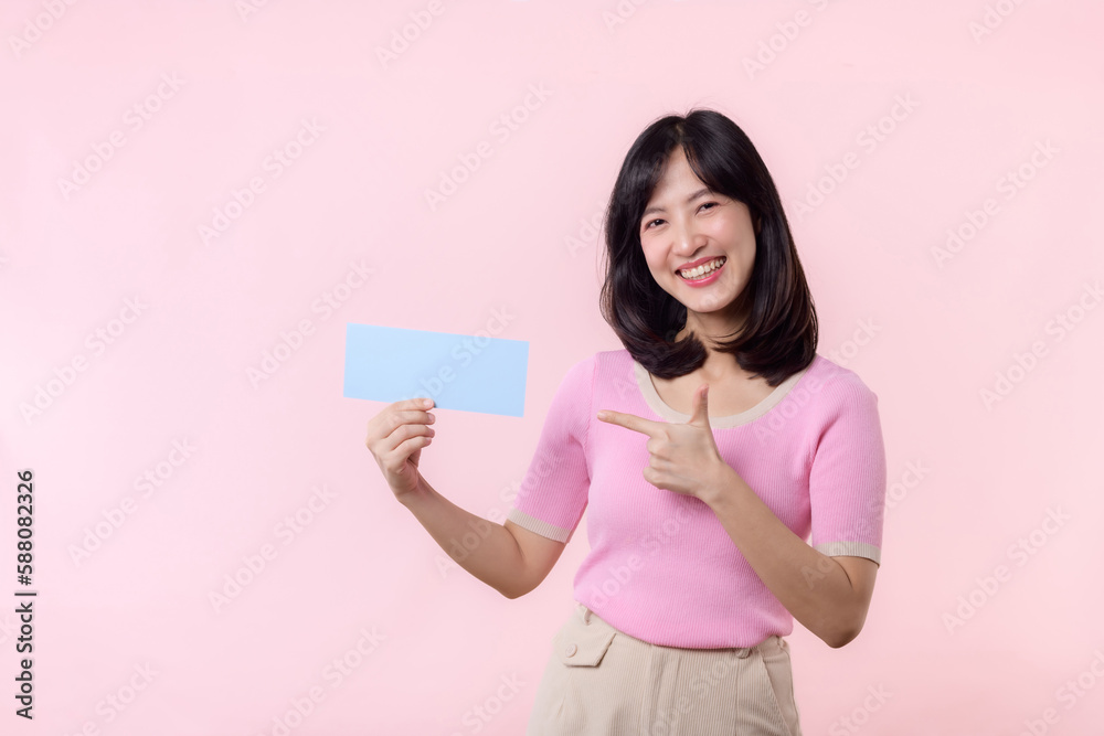 Portrait happy young woman model holding and showing blank space paper for advertisement information message poster with thumb up or point finger gesture isolated on pink pastel studio background. Portrait happy young woman model holding and showing blank space paper for advertisement information message poster with thumb up or point finger gesture isolated on pink pastel studio background.