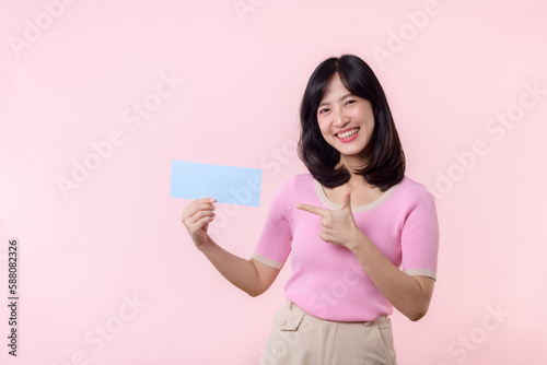 Portrait happy young woman model holding and showing blank space paper for advertisement information message poster with thumb up or point finger gesture isolated on pink pastel studio background.