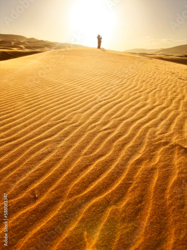 Dunes in the Sahara desert  Merzouga desert  grains of sand forming small waves on the dunes  panoramic view. Setting sun. Silhouette of a girl who takes a photo. Morocco