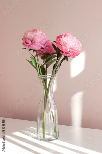 pink peonies in a glass vase on a white table surface