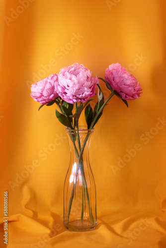 pink peonies in a glass vase against the background of yellow curtains