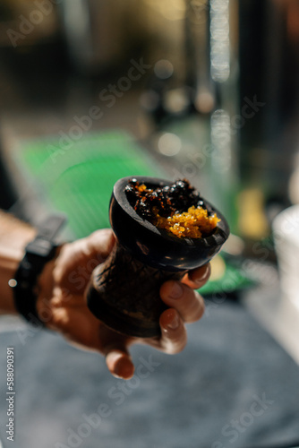 close-up of hand holding aromatic juicy yellow tobacco in hookah bowl Preparing hookah in lounge bar