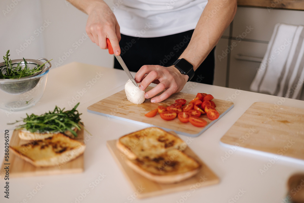Man slice peace of mozzarella on wooden board. Preparing Italian classic sandwich