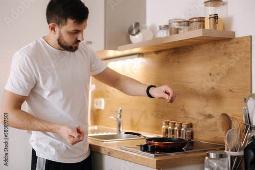 Handsome man preparing food at home. Young male surprise his beloved woman and make breakfast on kitchen. Salt the dish