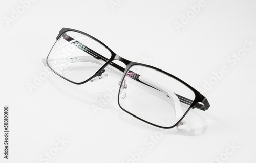 Glasses in a black metal frame are reflected in a white mirror background and have glare on the lenses