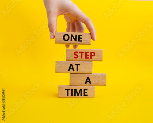 One step at a time symbol. Concept words One step at a time on wooden blocks. Beautiful yellow background. Businessman hand. Business and One step at a time concept. Copy space.