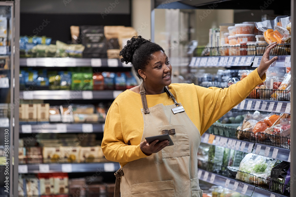 Waist up portrait of smiling black woman working in supermarket and wearing apron, copy space