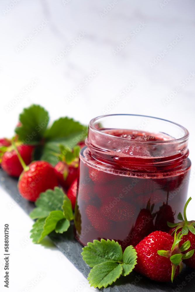 Strawberry sauce in glass jar on slate dish with fresh strawberry fruit and green leaves on marble. Recipe of delicious berry sauce of strawberry full of vitamins and antioxidants. Strawberry sauce in glass jar on slate dish with fresh strawberry fruit and green leaves on marble. Recipe of delicious berry sauce of strawberry full of vitamins and antioxidants.