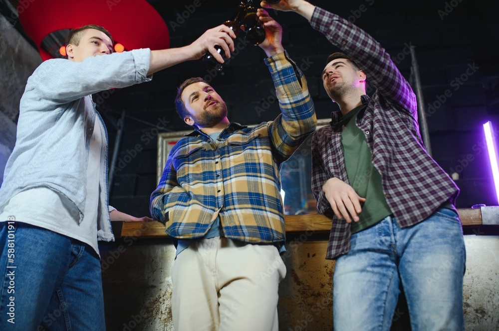 Fototapeta premium Old friends meeting. Happy young men in casual wear toasting with beer while sitting in beer pub together