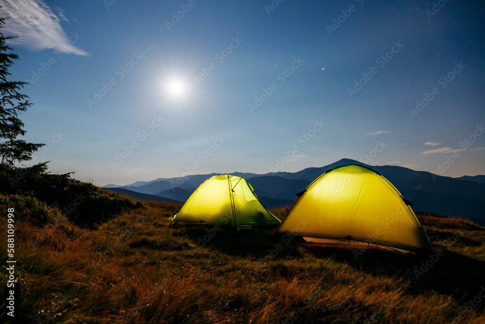 The two tents in the foreground is highlighted from the inside. Carpathian mountains, Ukraine, Europe.