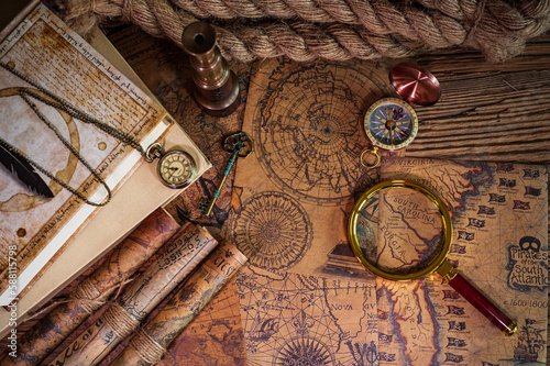 Old objects, book, magnifying glass, compass, pocket watch, spyglass, thick rope, old key lying on old maps in flat lay view