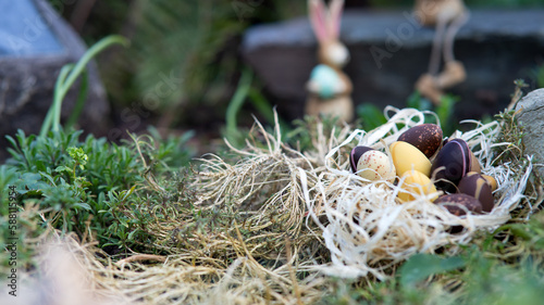 Easter chocolate eggs in the nest hidden in the garden with two small bunny’s in the background.