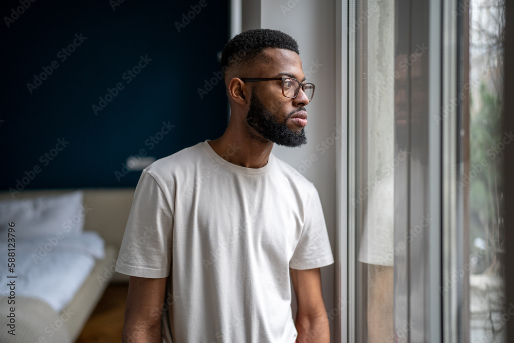 Sad Black man looking out of window thinking about life problems. Lonely African American guy at home dealing with breakup depression. Worried male pondering before making decision. Loneliness concept Sad Black man looking out of window thinking about life problems. Lonely African American guy at home dealing with breakup depression. Worried male pondering before making decision. Loneliness concept