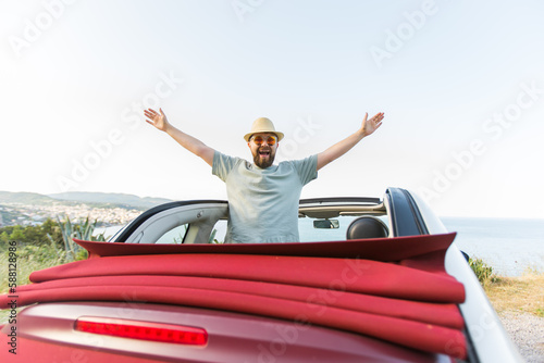 Happy man sitting in white convertible car with beautiful view and having fun - travel summer vacation and rental car concept