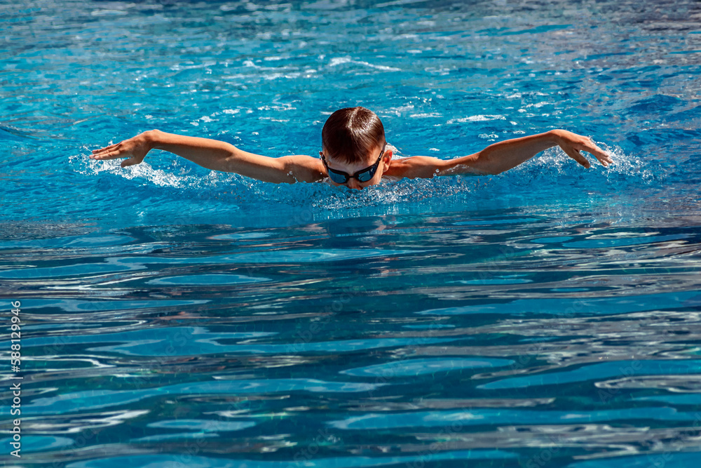 Boy child swimmer swims in swimming pool with butterfly style. Water sports, training, competition, activities, learn to swim school classes for children
