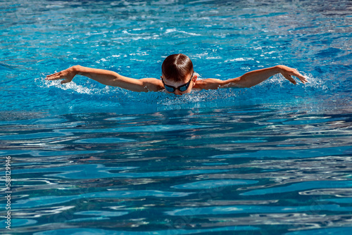 Boy child swimmer swims in swimming pool with butterfly style. Water sports, training, competition, activities, learn to swim school classes for children photo