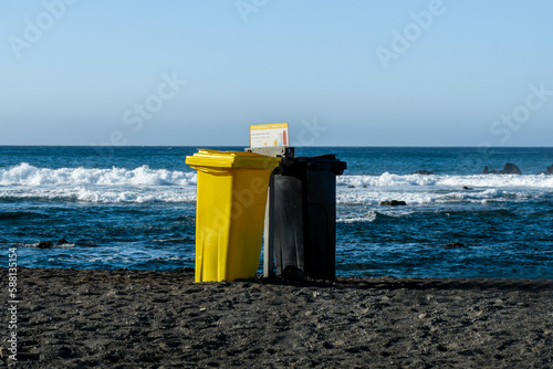 Reciclying bins for plastic and glass and informative poster in a beautiful rocky beach with black sand in Las Galletas, coast of Tenerife photo