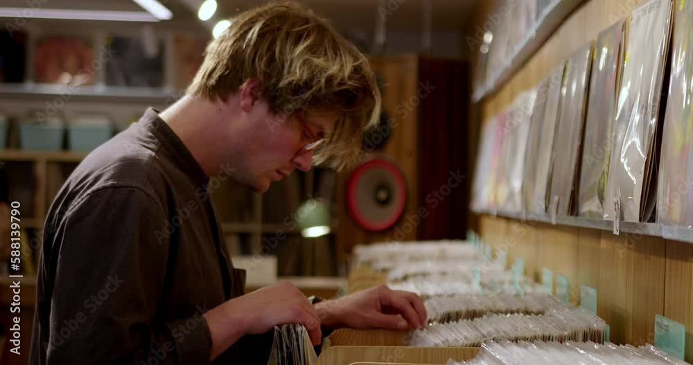 A stylish hipster man chooses vinyl records in a music store as a gift for a music collection. A DJ buys music for a party. A fashionable guy is looking for music on vinyl records in a vintage store A stylish hipster man chooses vinyl records in a music store as a gift for a music collection. A DJ buys music for a party. A fashionable guy is looking for music on vinyl records in a vintage store