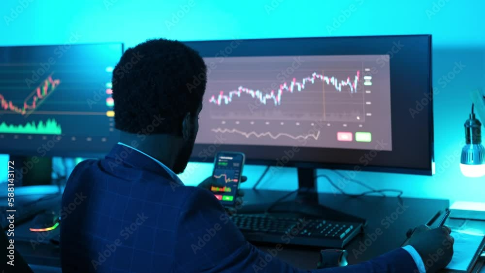 Young man in a suit investing with the mobile and checking the graphs to make profitable investments. Concept: Technology, business, profitability Young man in a suit investing with the mobile and checking the graphs to make profitable investments. Concept: Technology, business, profitability