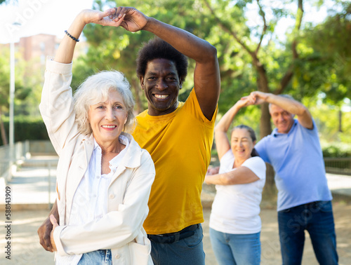 Two couples of mixed-race men and women of different age dancing outdoors in a park on sunny day